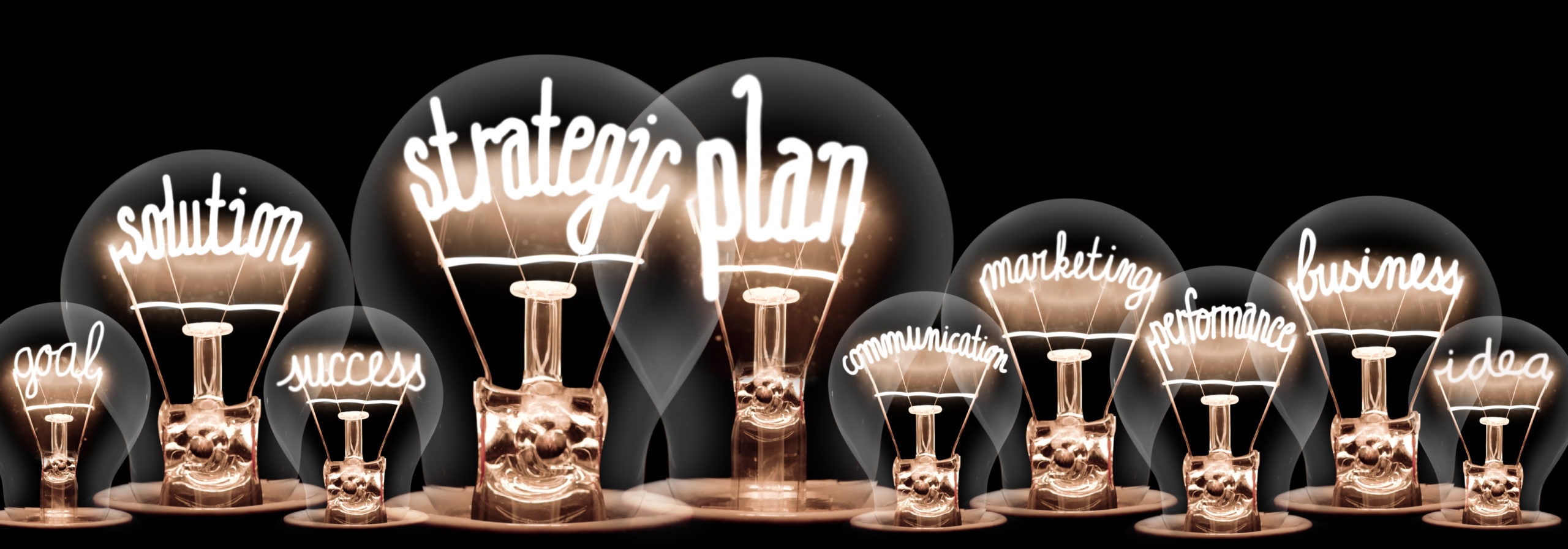 Group of light bulbs with shining fibers in a shape of Strategic Plan, Solution, Success and Idea concept related words isolated on black background